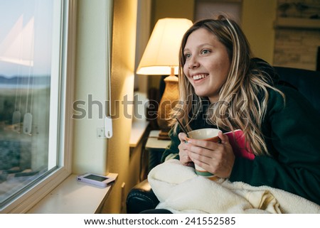 Young Blond Girl Sitting in Chair with book looking out the window and smiling