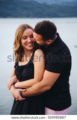 Beautiful Couple River Background Guy Hugging from behind kissing cheek