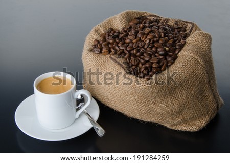 A cup of coffee with coffee beans in a burlap bag, on grey background