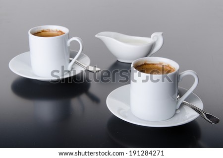 Two cups of coffee with a milk jug, on grey background
