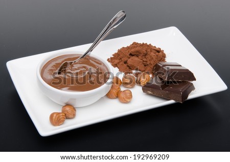 Composition of chocolate hazelnut spread, hazelnuts, chocolate and cocoa on a black background