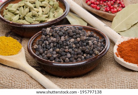 Composition of wooden spoons and cups with cardamom, pepper, paprika, pink peppercorn and curry on a burlap bag
