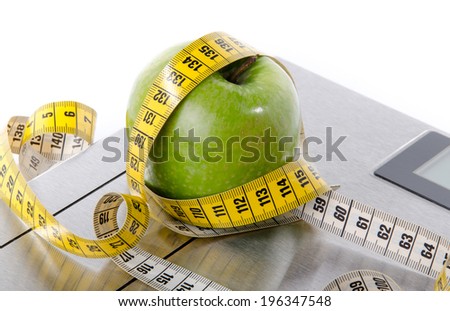 Tape measure around a green apple on a bathroom scales, isolated on white