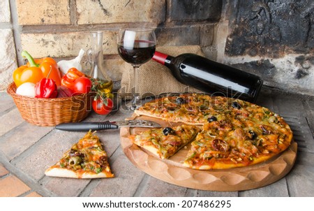 Composition with a pizza, wine and some ingredients on a firebricks background
