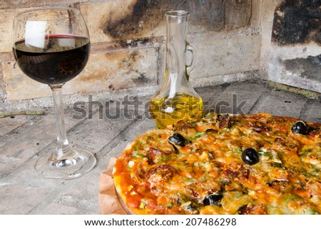 Composition with a pizza, wine and oil on a firebricks background