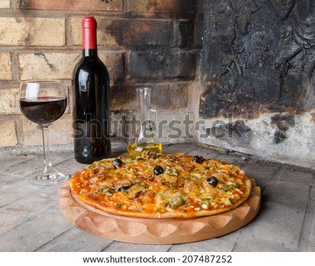 Composition with a pizza, wine and oil on a firebricks background