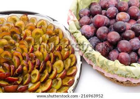Plum tart before baking and a basket with fresh plums, isolated on white