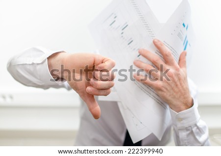 Stressed businessman, thumb down, holding bad graphs against his face