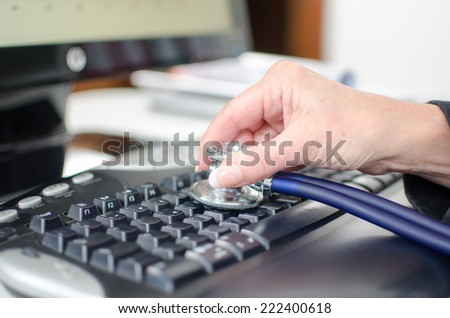 Woman\'s hand checking a keyboard with a stethoscope, closeup