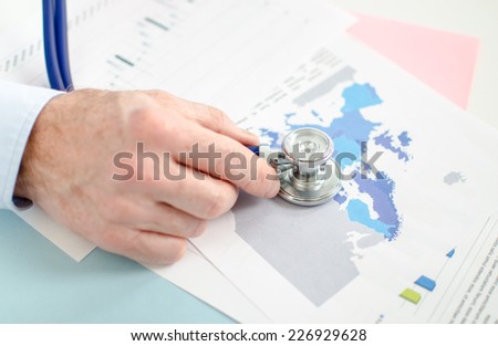 Businessman analyzing an economic document with a stethoscope, closeup
