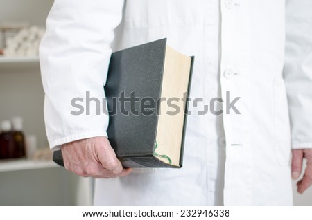 Doctor holding a medical book under his arm in his office