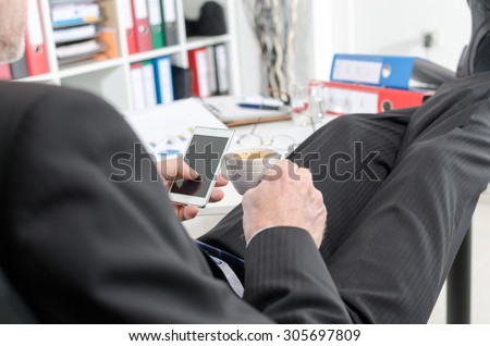 Relaxed businessman during a break drinking coffee and using his smartphone