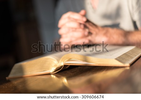Man praying hands on a Bible in dim light
