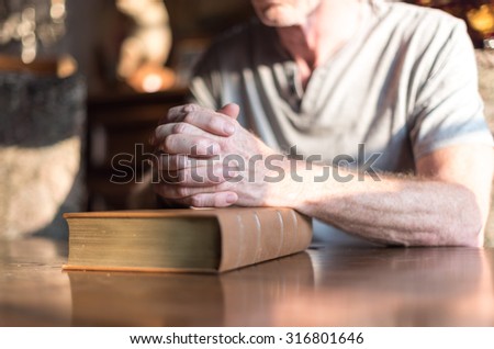 Man sitting at a table praying hands on a Bible