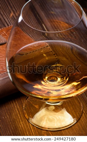 Luxury still life with glass of cognac and leather wallet on a wood background. Top view