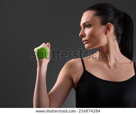Fitness woman working out with green dumbbell looking at the side on dark background. Fitness concept