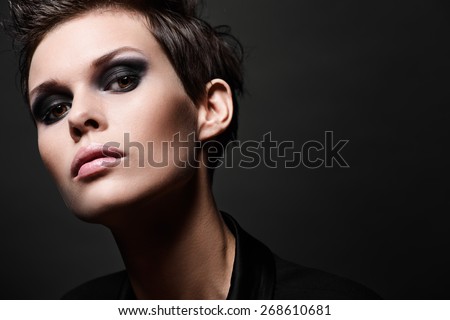 Fashion head shot of brunette woman with short hair cut on black background. Smokey eyes make up