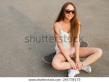 Young woman sitting on the skateboard in casual street wear and sun glasses