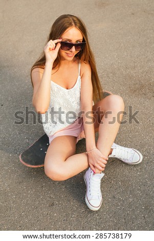 Young woman posing on the skateboard in casual street wear and sun glasses