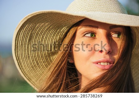 Young  smiling beauty woman in summer hat over green background. Half face shot. Model looking at the side