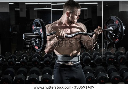 Athlete muscular bodybuilder in the gym training biceps with bar.