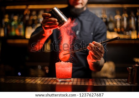 Barman adding spices powder into a cocktail glass filled with a fresh strong alcoholic cocktail with slice of lemon