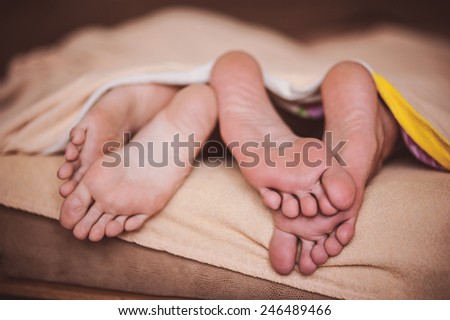 couple barefoot in bed under blanket no face