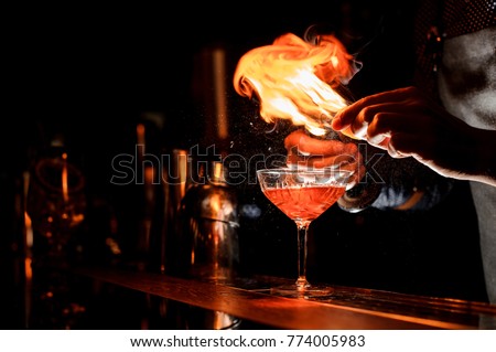 Barman`s hands making a fresh alcoholic cocktail with a smoky note on the dark bar counter