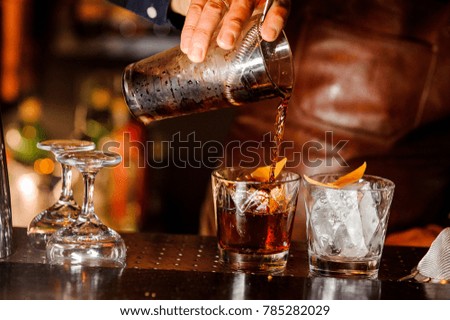 Barman pouring fresh alcoholic drink into the glasses with ice cubes on the bar counter