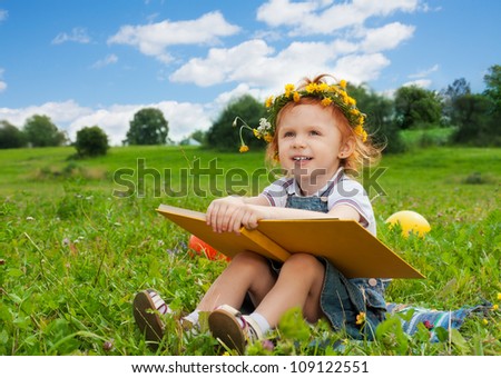 funny little girl reading book on the grass
