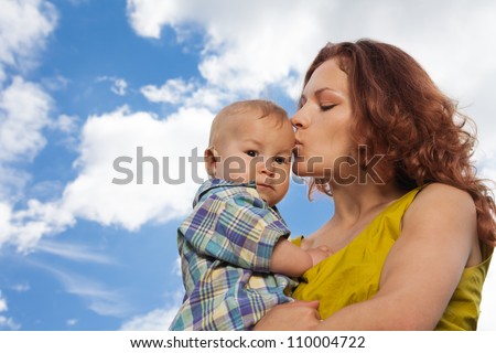mother kissing her adorable baby on cloudy background