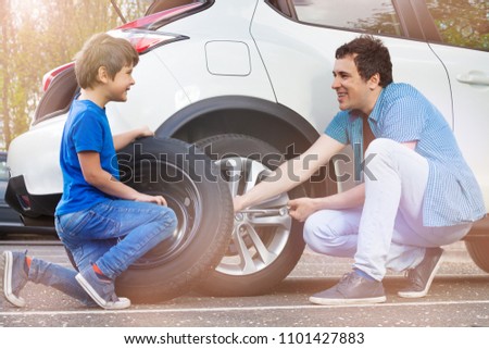 Happy father and son changing wheels on car