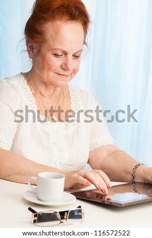Portrait of old lady in her 60s holding tablet and exploring new features