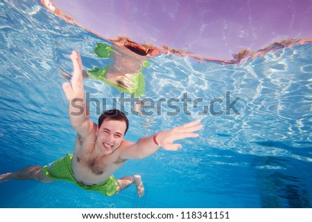 Happy man diving underwater in the pool with wide smile