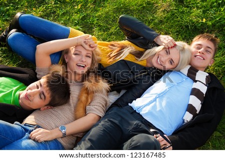 Group of four young people - two couples laying in the grass with smile no their faces