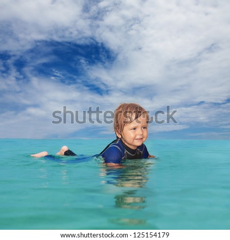 Little boy laying in the water wearing a wet suit
