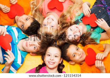 Kids laying in circle with hearts in their hands smiling, boys and girls with diversity