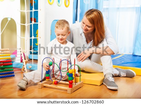 Mothers and her little blond boy learning to solve puzzle with toys