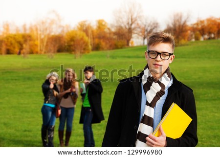 Smart student with friends holding a book and wearing glasses on the loan in park
