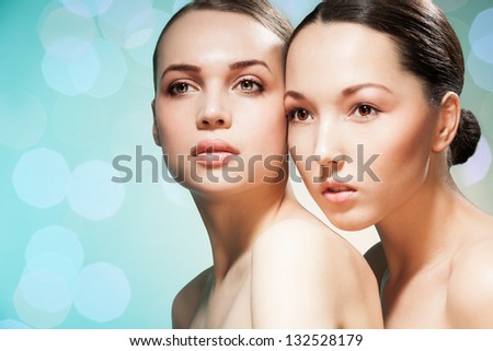 Beauty portrait of two women Asian and Caucasian on blurry blue abstract background