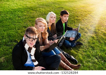 Four students sitting with laptops in the park on the grass