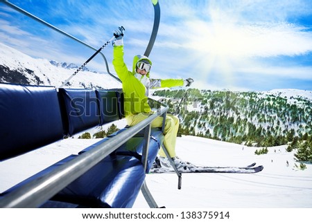 Happy young woman skier on ski lift with smile and lifted happy hands