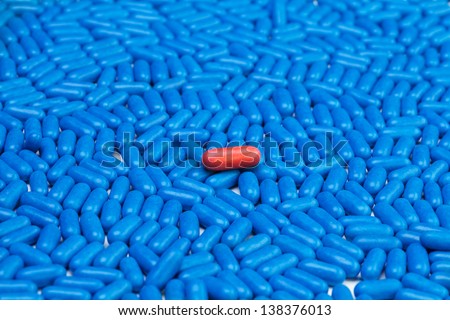 One red drug pill laying on many blue tablets