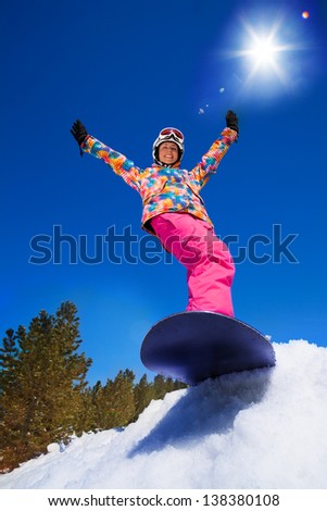 Happy smiling girl with lifted hands stand on snowboard about to slide downhill the mountain