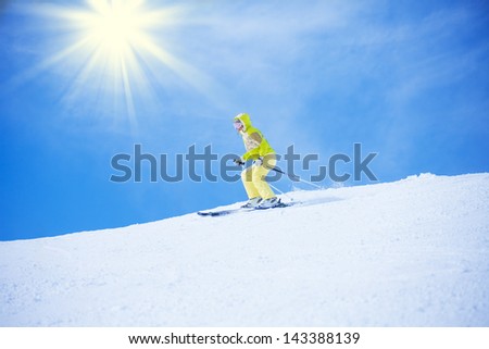 Young happy woman sliding downhill with clean white snow and blue sky with sun on background