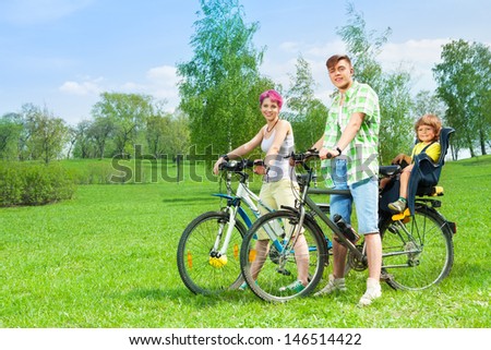 Young family man and woman on the bikes with kid in child seat riding together in the park