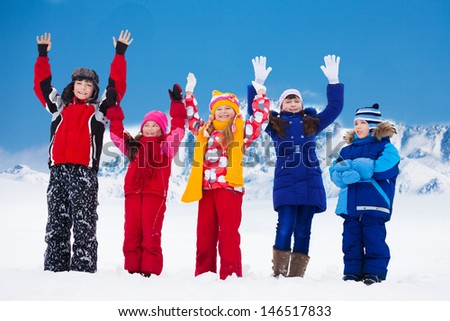Group of five super happy kids standing in snow with lifted hands
