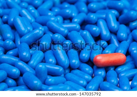 Close shoot of one red drug pill laying on many blue tablets