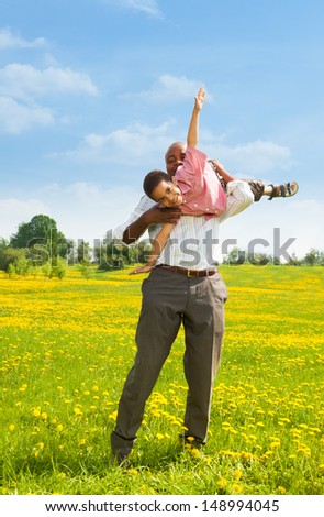 Black father playing with little boy holding him in airplane pose in the park