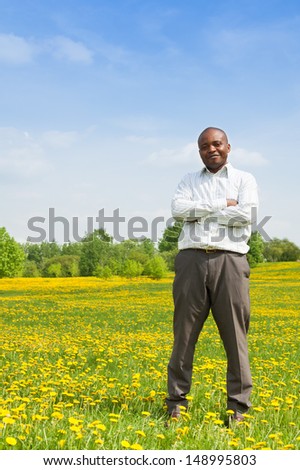 Happy confident black man wearing shirt standing outside in the park on the yellow dandelion field